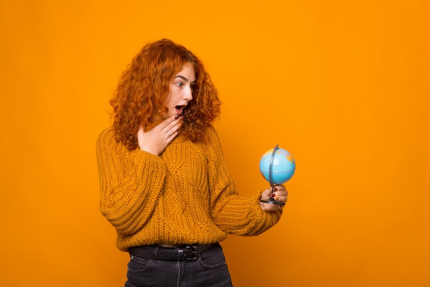 Jeune femme cherche surpris au globe sur le mur orange.