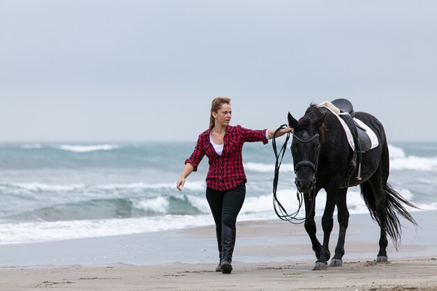 Jeune femme sur un cheval sur la plage un jour nuageux