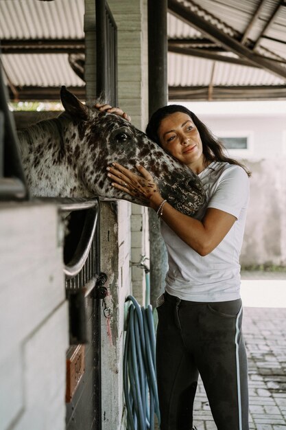 Une jeune femme et un cheval, des sentiments, des soins, de l'affection, de la tendresse, une femme câline et embrasse un cheval. Gros plan d'une jeune femme heureuse étreignant son cheval.