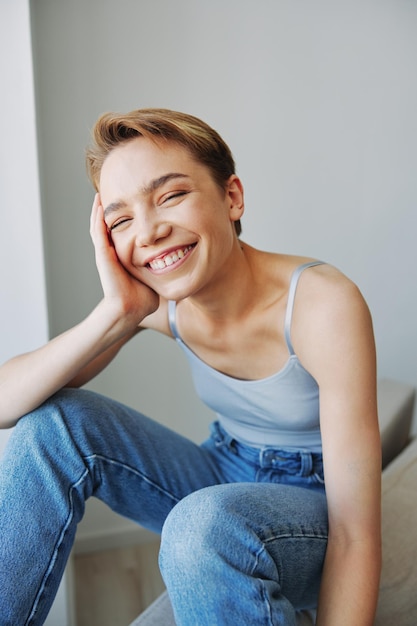 Jeune femme avec des cheveux courts se divertissant à la maison sur le canapé sourire et bonheur vacances à la maison poser naturel sans filtres espace de copie gratuit photo de haute qualité