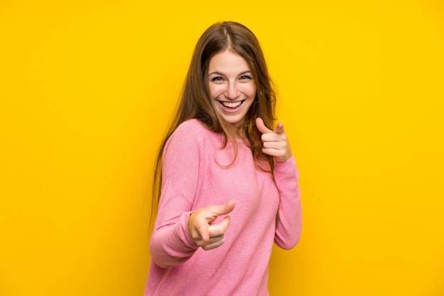 Jeune femme avec des cheveux longs sur un mur jaune isolé pointant vers l&#39;avant et souriant