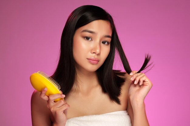 Une jeune femme avec des cheveux longs stylés devant un fond coloré pendant une routine de beauté