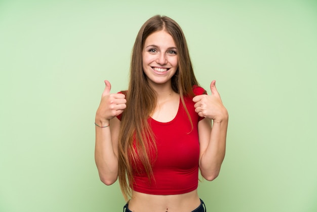 Jeune femme, à, cheveux longs, sur, vert, mur, isolé, donner, a, pouces haut geste