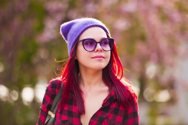 Jeune femme chic avec des cheveux de couleur fuchsia brillant regardant à travers des lunettes violettes. Concept de vie coloré. Ville estompée sur fond