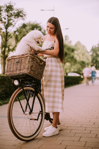 Jeune femme avec un chien bichon blanc frisé dans le panier du vélo électrique