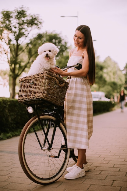 Jeune femme avec un chien bichon blanc frisé dans le panier du vélo électrique