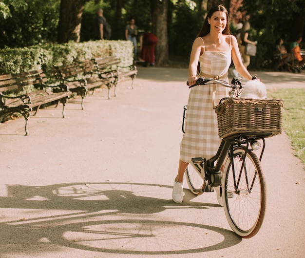 Jeune femme avec un chien bichon blanc frisé dans le panier du vélo électrique