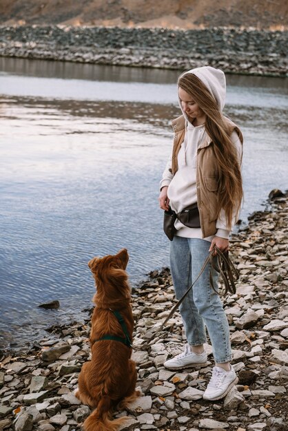 Jeune femme et chien retriever marche sur la rive de la rivière à la saison d'automne