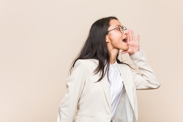 Jeune femme chinoise d'affaires criant et tenant la paume près de la bouche ouverte.