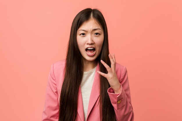 Jeune femme chinoise d'affaires portant un costume rose criant de rage.