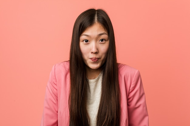 Jeune femme chinoise d'affaires portant un costume rose hausse les épaules et les yeux ouverts confus.