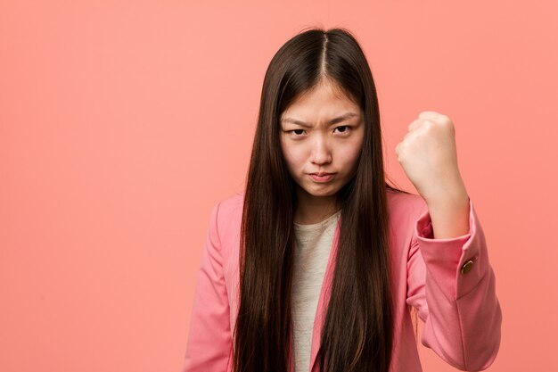 Jeune femme chinoise d'affaires portant un costume rose montrant le poing à la caméra, une expression faciale agressive.