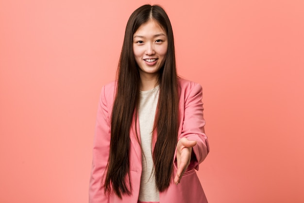 Jeune femme chinoise d'affaires portant un costume rose qui s'étend de la main à la caméra dans le geste de salutation.