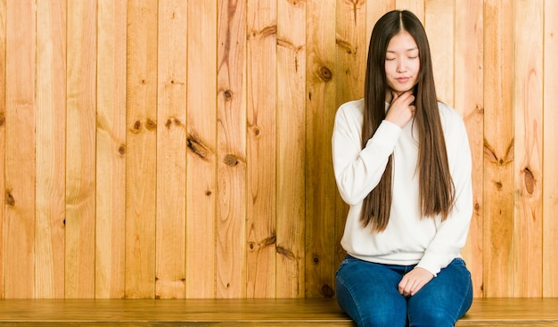 Jeune femme chinoise assise sur une place en bois souffre de douleurs dans la gorge en raison d'un virus ou d'une infection.