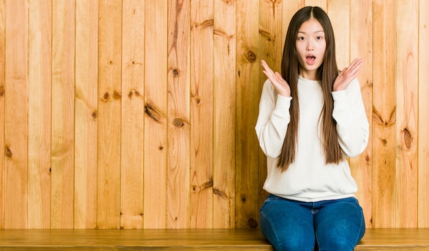 Jeune femme chinoise assise sur une place en bois surprise et choquée.