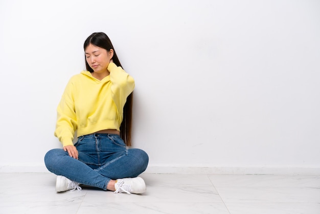 Jeune femme chinoise assise sur le sol isolé sur mur blanc avec mal de cou