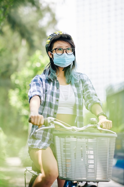 Jeune femme chinoise en casque et masque médical à vélo en ville