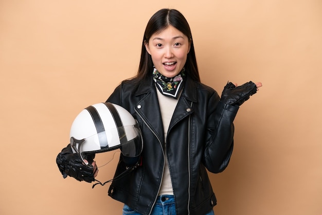 Jeune femme chinoise avec un casque de moto isolé sur fond beige avec une expression faciale choquée