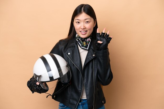 Jeune femme chinoise avec un casque de moto isolé sur fond beige heureux et comptant quatre avec les doigts