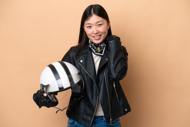 Jeune femme chinoise avec un casque de moto isolé sur fond beige en riant