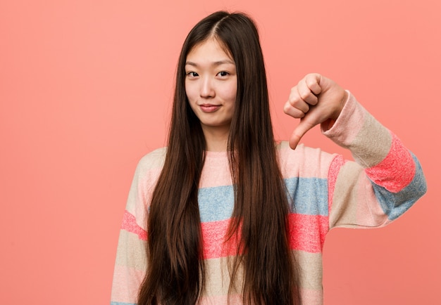 Jeune femme chinoise cool montrant un geste d'aversion, les pouces vers le bas. Concept de désaccord.