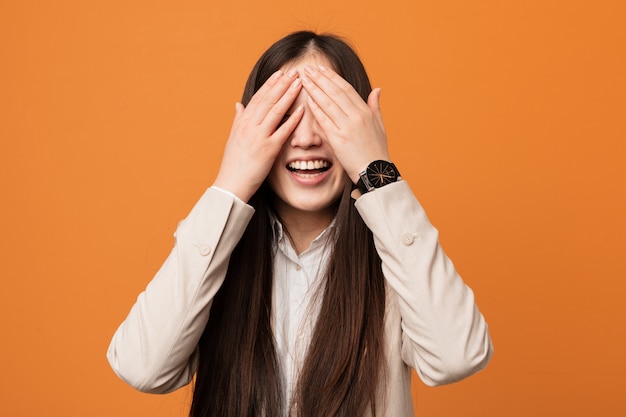 Jeune femme chinoise couvre les yeux avec les mains, sourit largement en attendant une surprise.