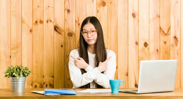 Jeune femme chinoise étudiant sur son bureau, pointe de côté, essaie de choisir entre deux options.