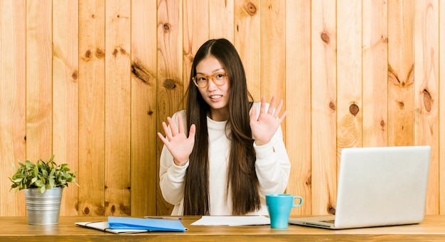 Jeune femme chinoise étudiant sur son bureau, rejetant une personne montrant un geste de dégoût.