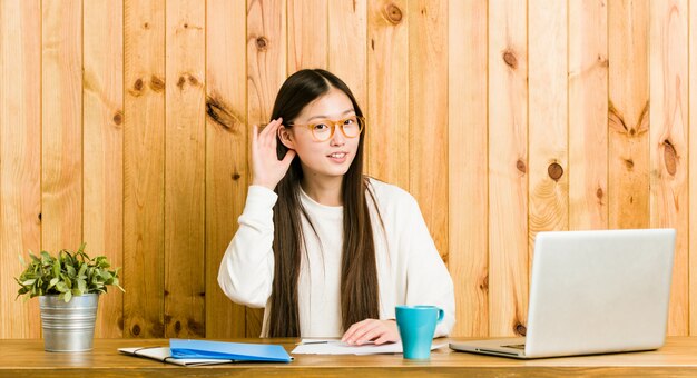 Jeune femme chinoise étudie son bureau en essayant d'écouter un commérage.