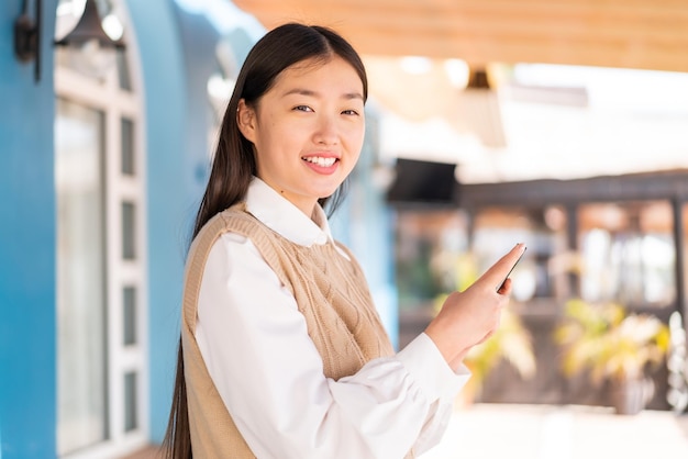 Jeune femme chinoise à l'extérieur envoyant un message ou un e-mail avec le mobile