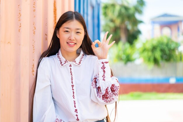 Jeune femme chinoise à l'extérieur montrant le signe ok avec les doigts