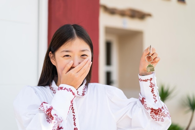 Jeune femme chinoise à l'extérieur tenant les clés de la maison avec une expression heureuse