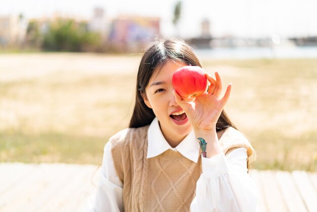 Jeune femme chinoise à l'extérieur tenant une pomme avec une expression surprise