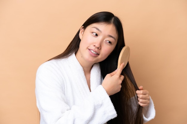 Jeune femme chinoise isolée sur fond beige avec un peigne à cheveux