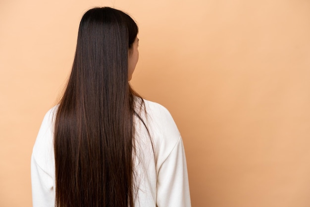 Jeune femme chinoise isolée sur fond beige en position arrière et regardant de côté