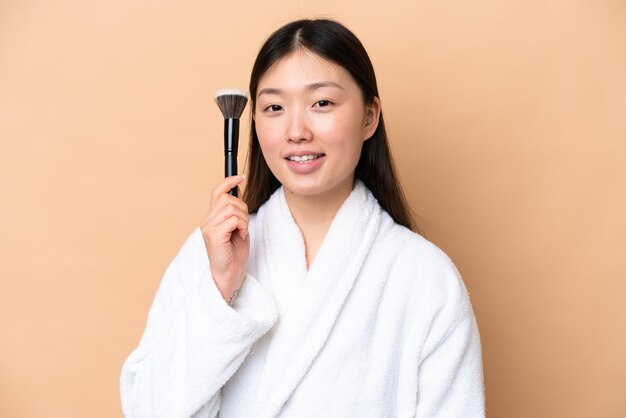 Jeune femme chinoise isolée sur fond beige tenant un pinceau de maquillage