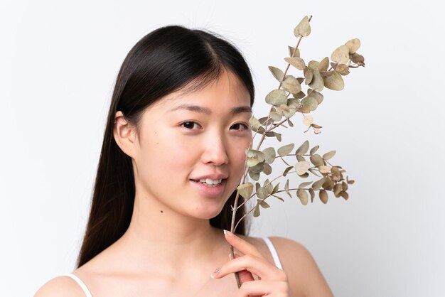 Jeune femme chinoise isolée sur fond blanc tenant une branche d'eucalyptus tout en souriant Close up portrait