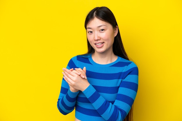 Jeune femme chinoise isolée sur fond jaune applaudissant