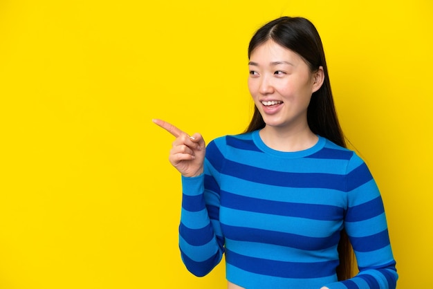 Jeune femme chinoise isolée sur fond jaune pointant le doigt sur le côté et présentant un produit