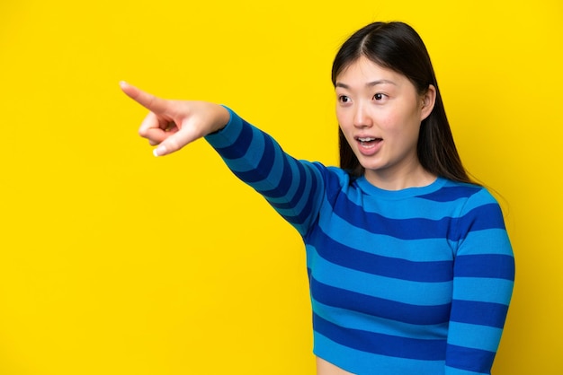 Jeune femme chinoise isolée sur fond jaune pointant vers l'extérieur