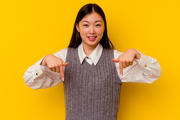 Jeune femme chinoise isolée sur fond jaune pointe vers le bas avec les doigts, sentiment positif.