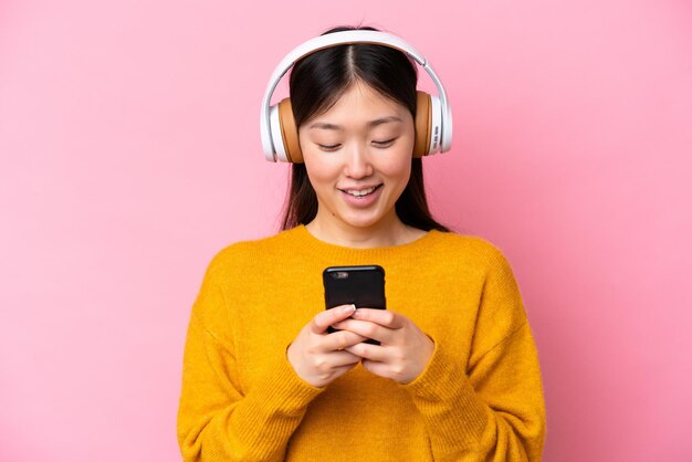 Jeune femme chinoise isolée sur fond rose écoutant de la musique et regardant vers le mobile