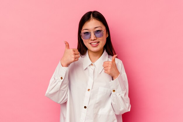 Jeune femme chinoise isolée sur fond rose levant les deux pouces vers le haut, souriante et confiante.