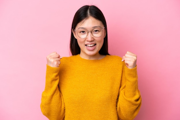 Jeune femme chinoise isolée sur fond rose avec des lunettes et célébrant une victoire