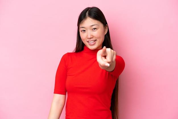 Jeune femme chinoise isolée sur fond rose pointant vers l'avant avec une expression heureuse