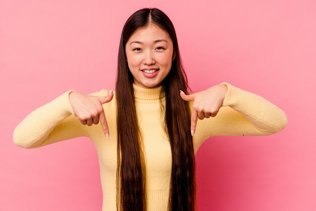 Jeune femme chinoise isolée sur fond rose pointe vers le bas avec les doigts, sentiment positif.