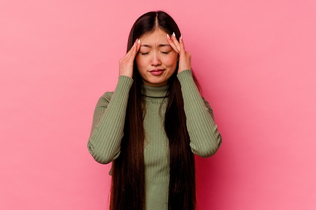 Jeune femme chinoise isolée sur fond rose touchant les tempes et ayant mal à la tête.