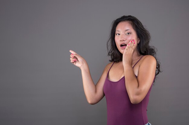 Jeune femme chinoise isolée avec un geste surpris pointant vers le côté indiquant quelque chose