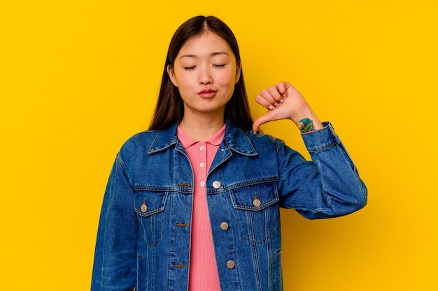 Jeune femme chinoise isolée sur jaune montrant un geste de dégoût, les pouces vers le bas. Concept de désaccord.