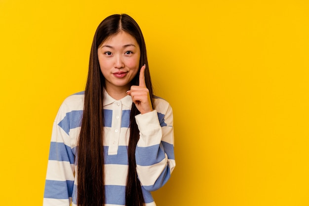 Jeune femme chinoise isolée sur jaune montrant le numéro un avec le doigt.